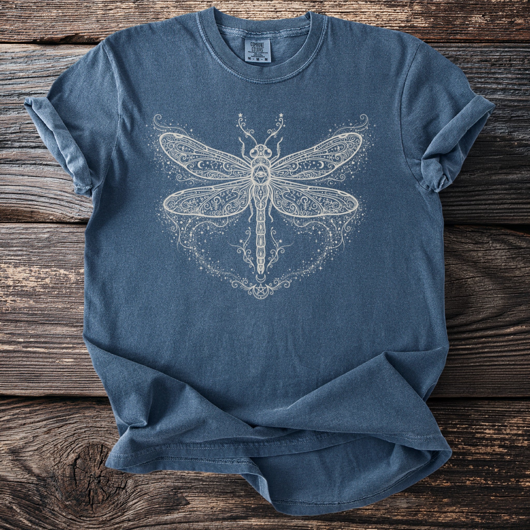 Blue t-shirt with white dragonfly and celestial graphic including stars and crescent moons.