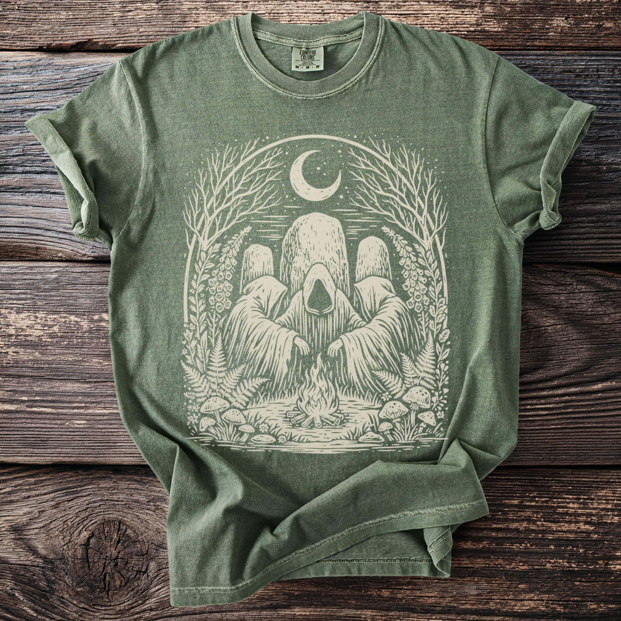 Green t-shirt with occult figures, campfire, moon, and nature elements design.
