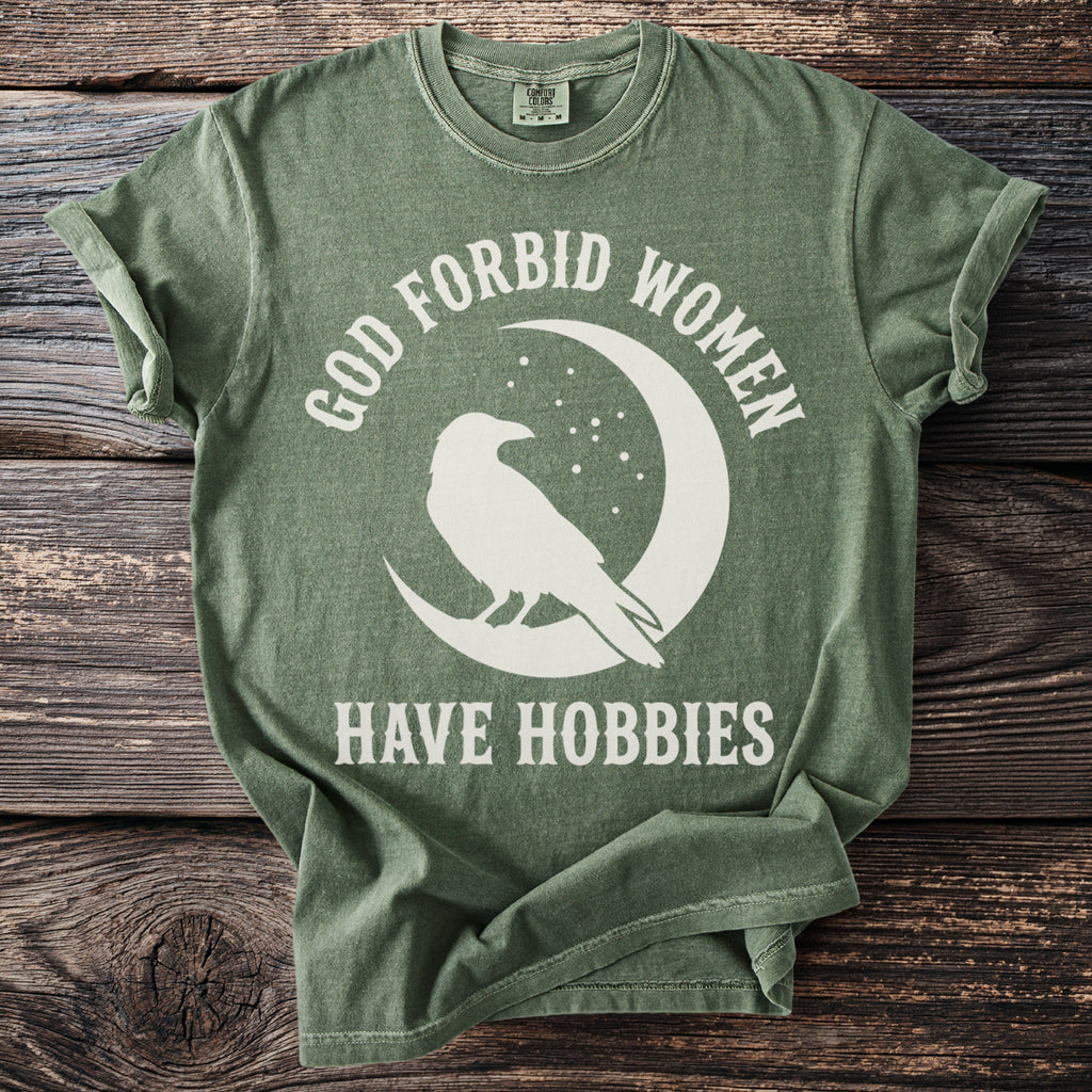 Green t-shirt with white text "GOD FORBID WOMEN HAVE HOBBIES" and a raven on a moon.