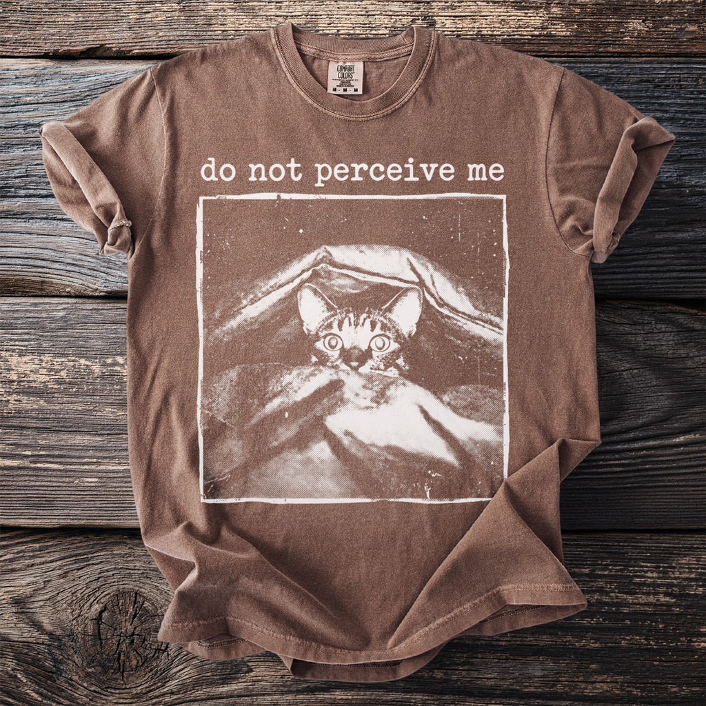 Brown t-shirt with a graphic of a cat peeking from under a blanket and "do not perceive me" text.