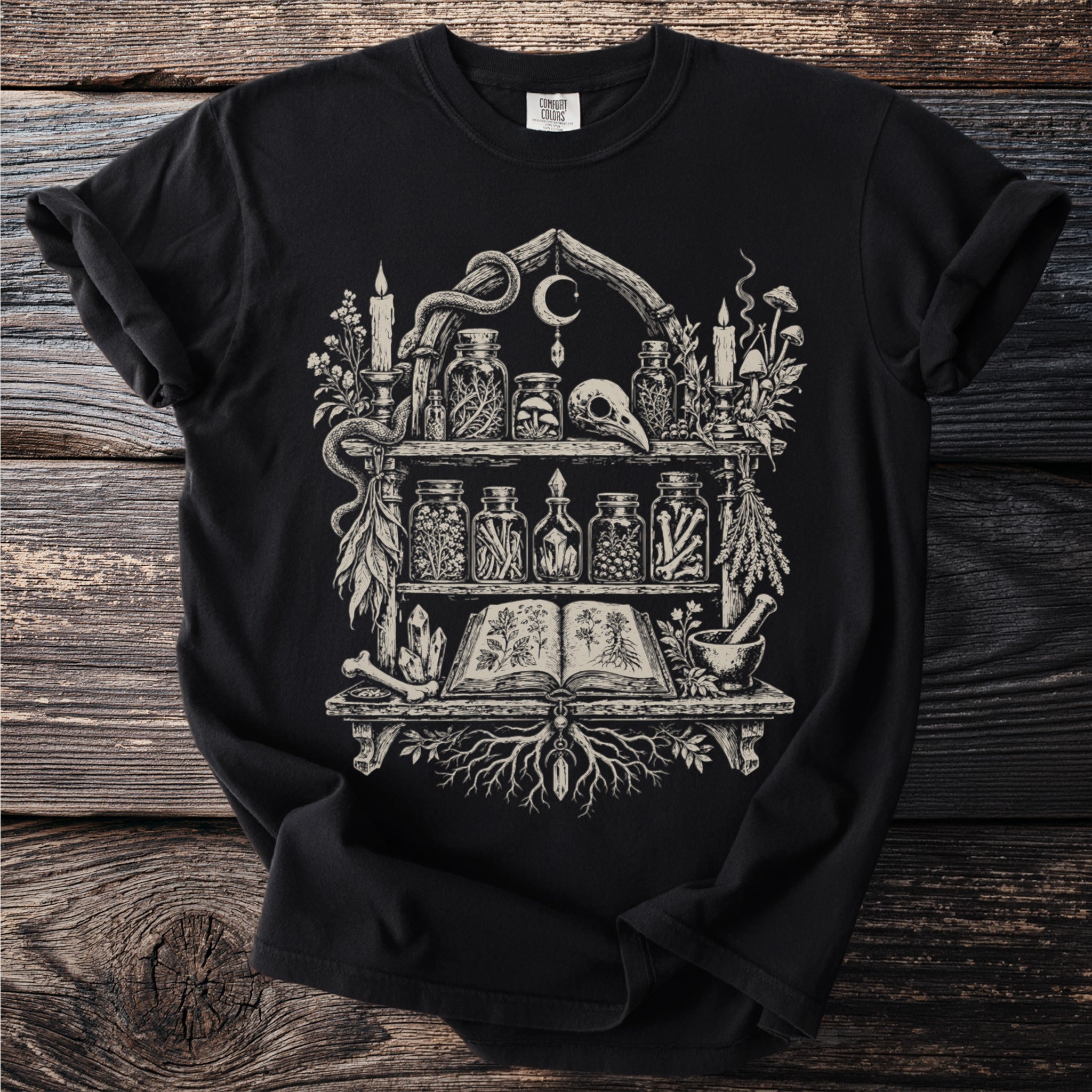 Black t-shirt with line art of an apothecary shelf filled with jars, books, and mystical items.