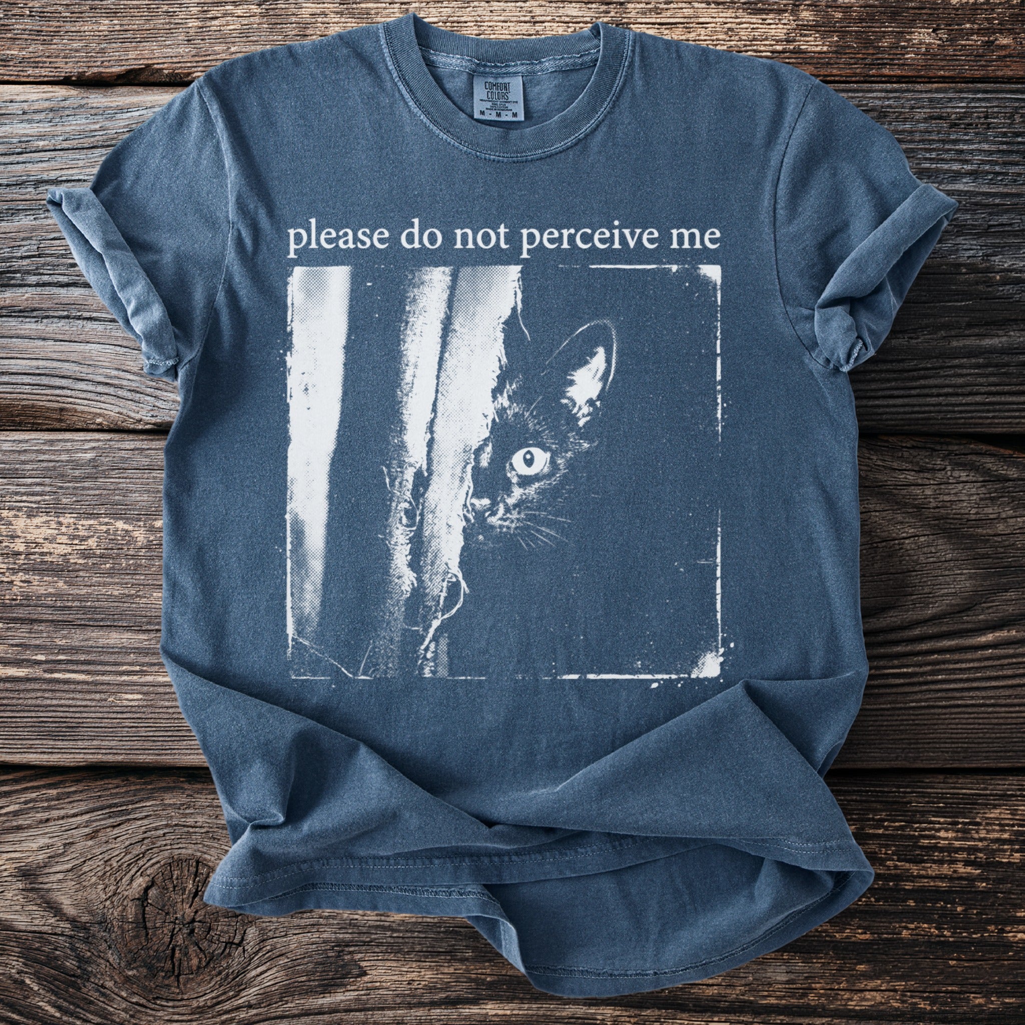 Blue t-shirt with "please do not perceive me" and a peeking cat graphic.