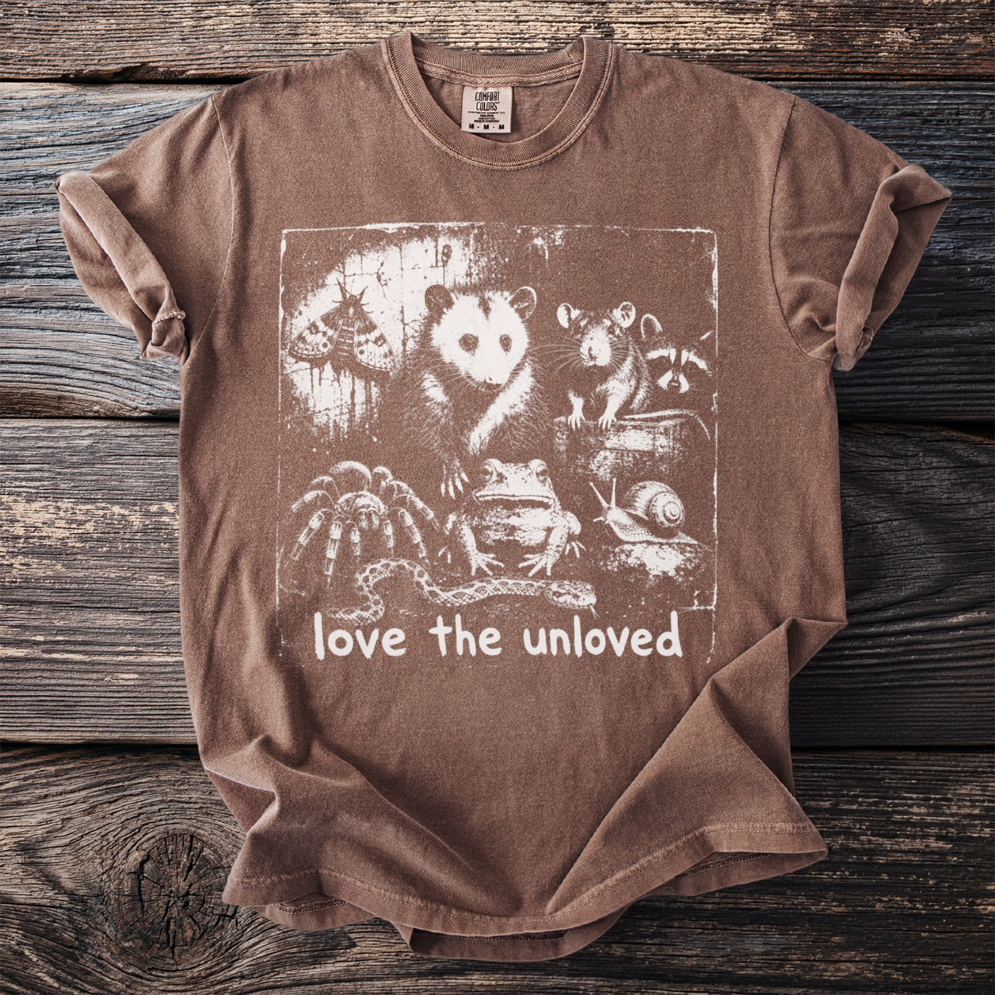 Brown t-shirt with white graphic of various creatures and text "love the unloved".
