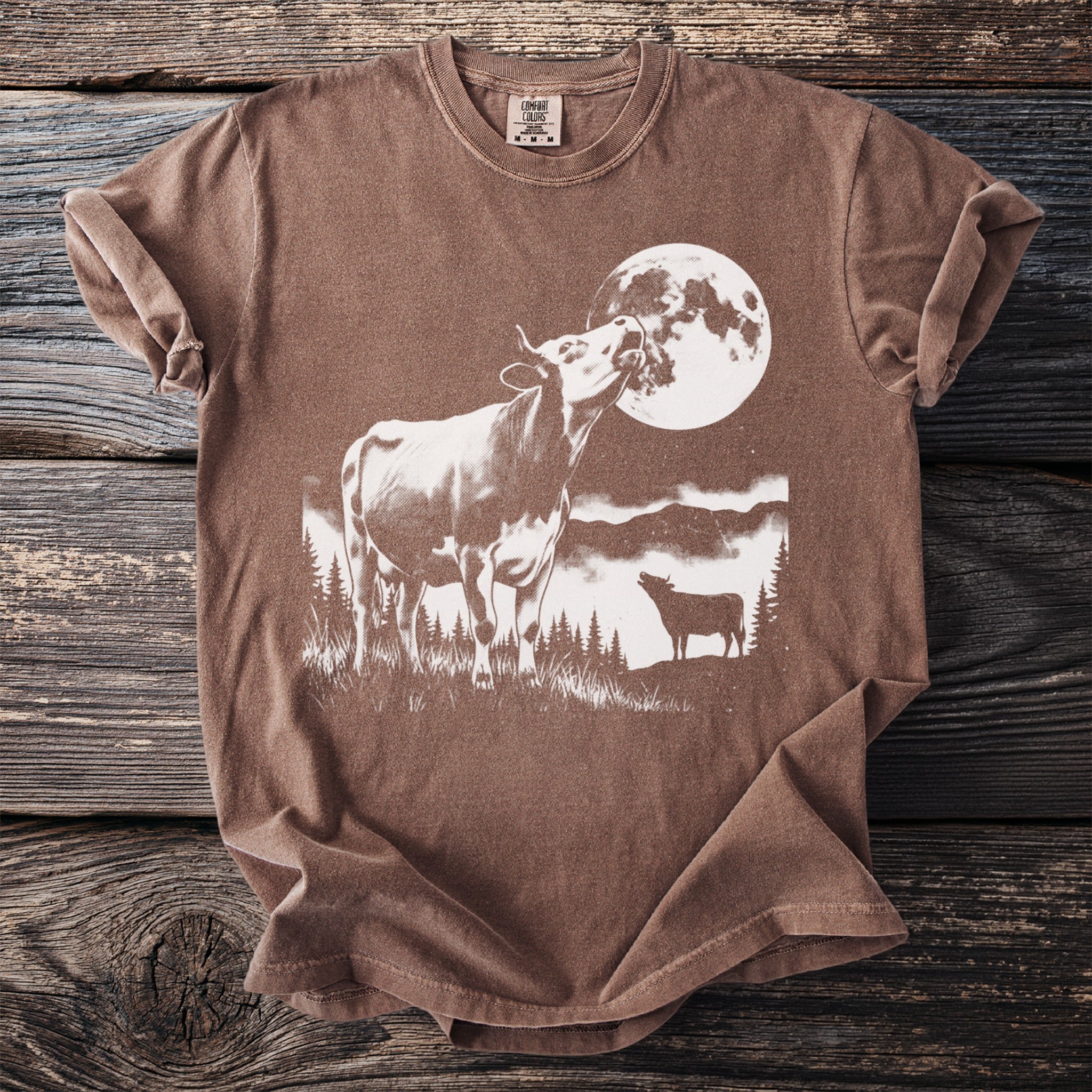 Brown t-shirt with white graphic of a cow mooing at the moon and another cow.
