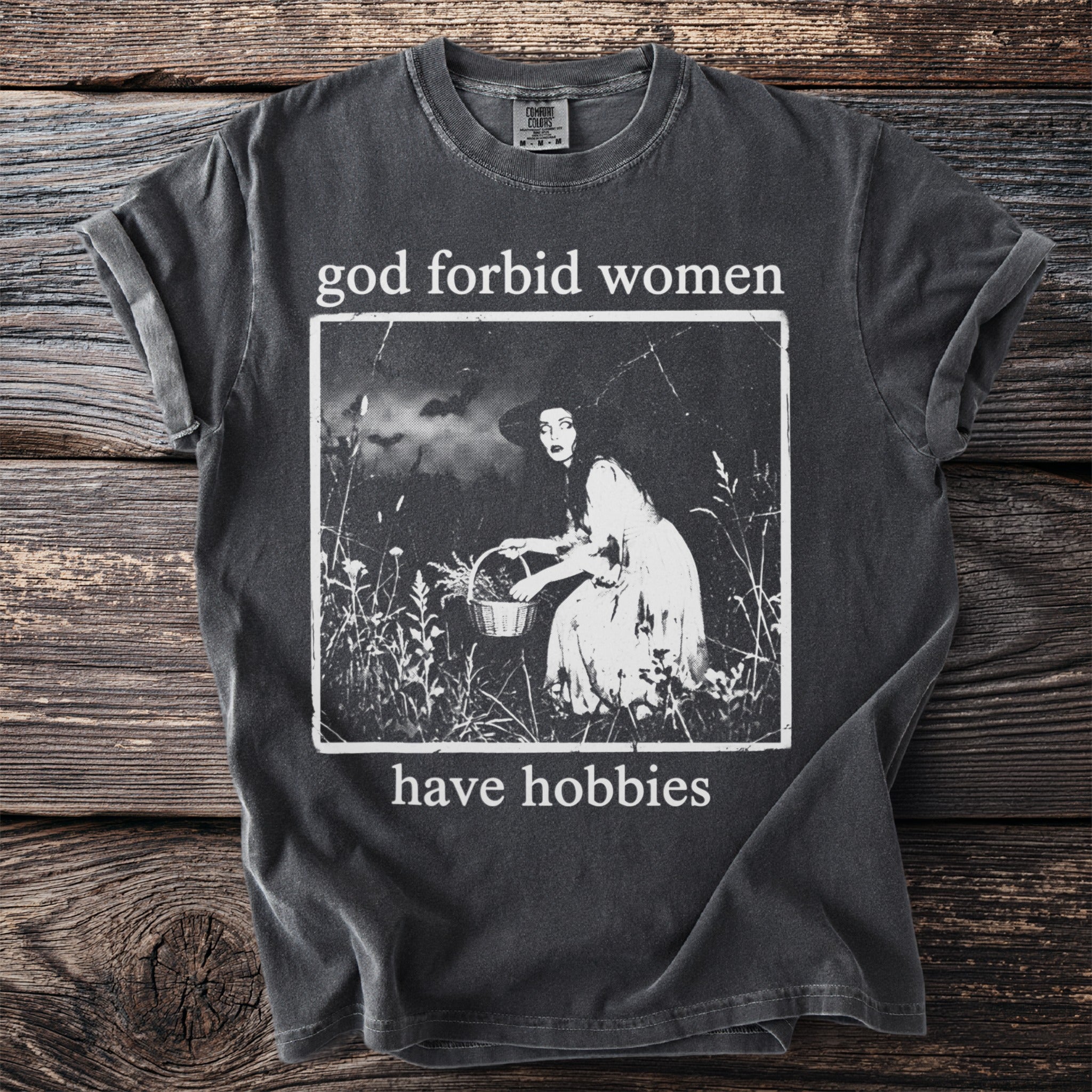 dark t-shirt with text "god forbid women have hobbies" and witchy graphic