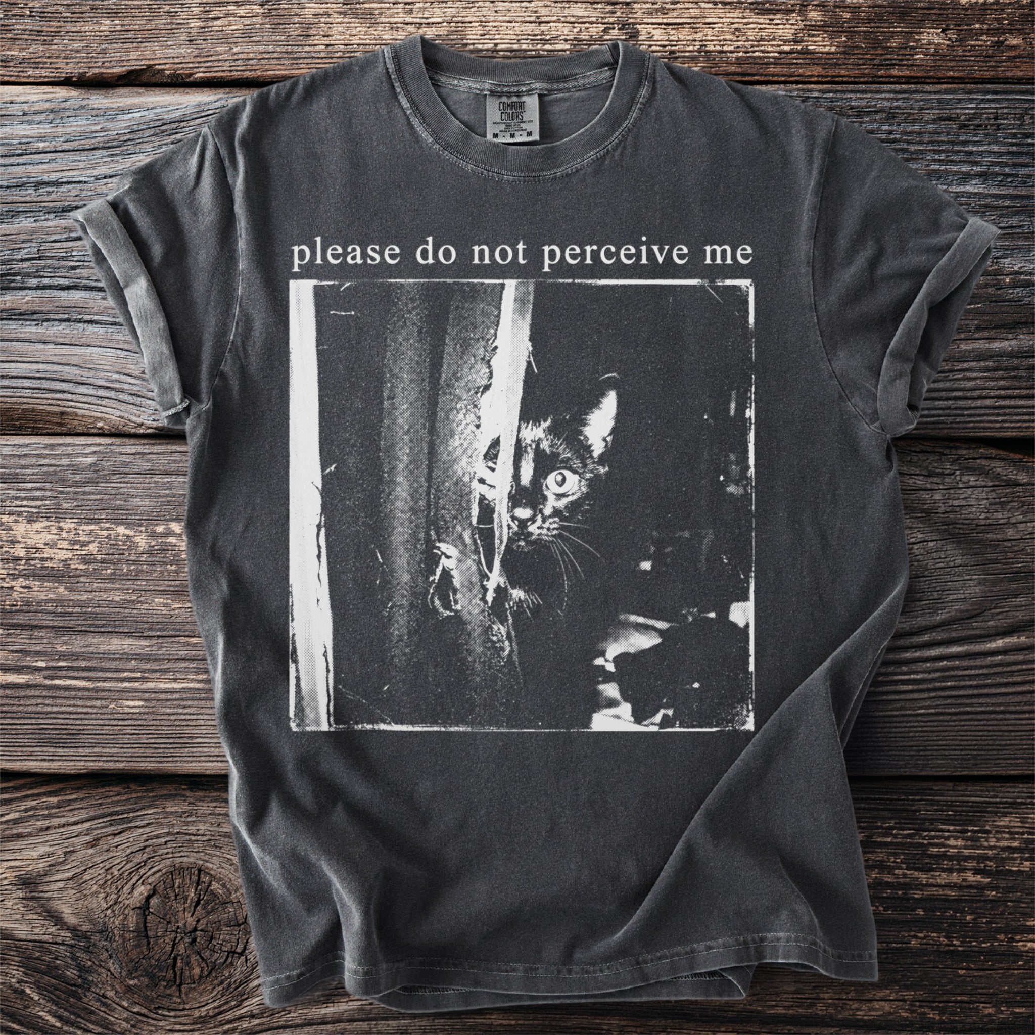Charcoal t-shirt with a black and white image of a cat peeking from behind fabric and text "please do not perceive me".