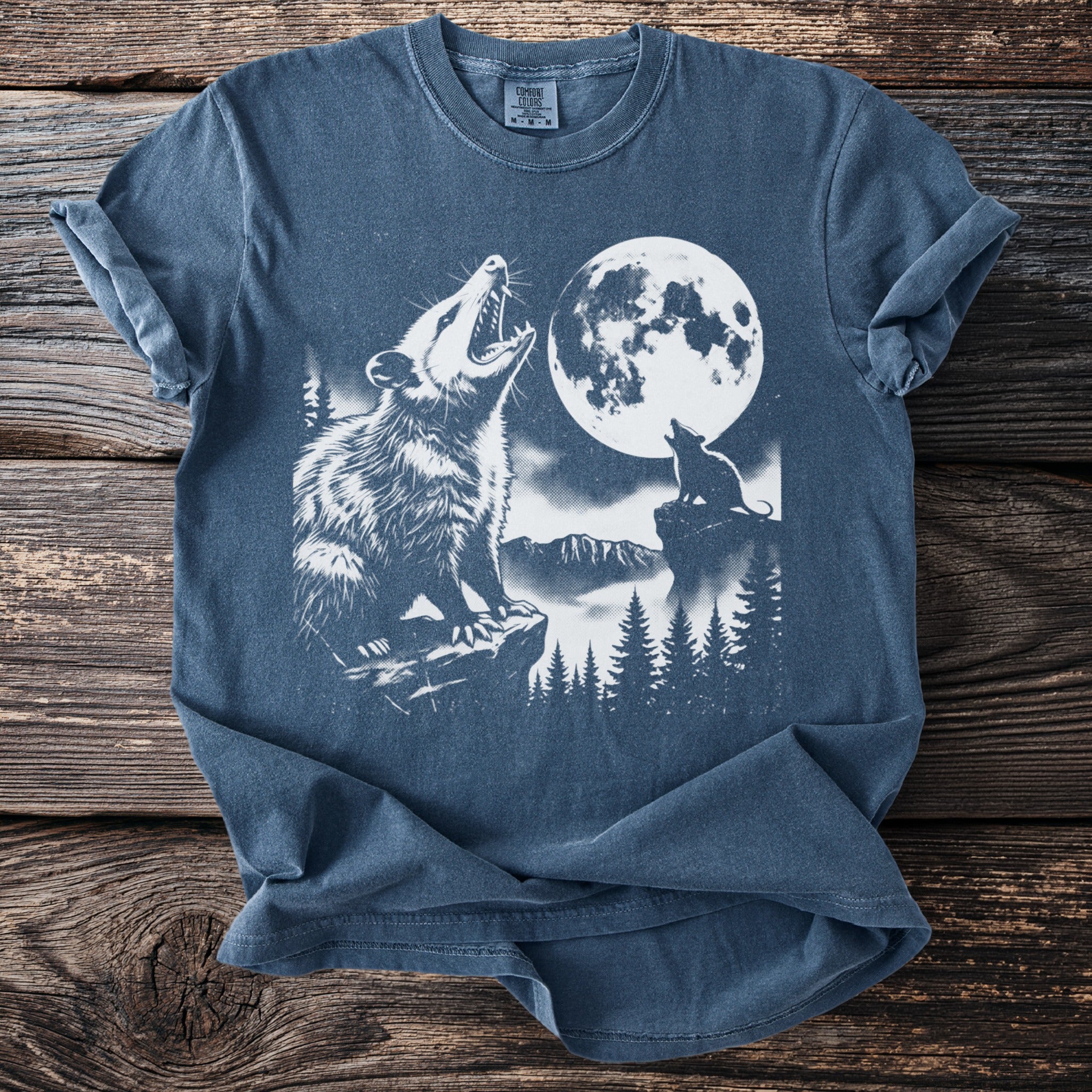 Opossum howling at moon with wolf in stylized forest scene on blue t-shirt.