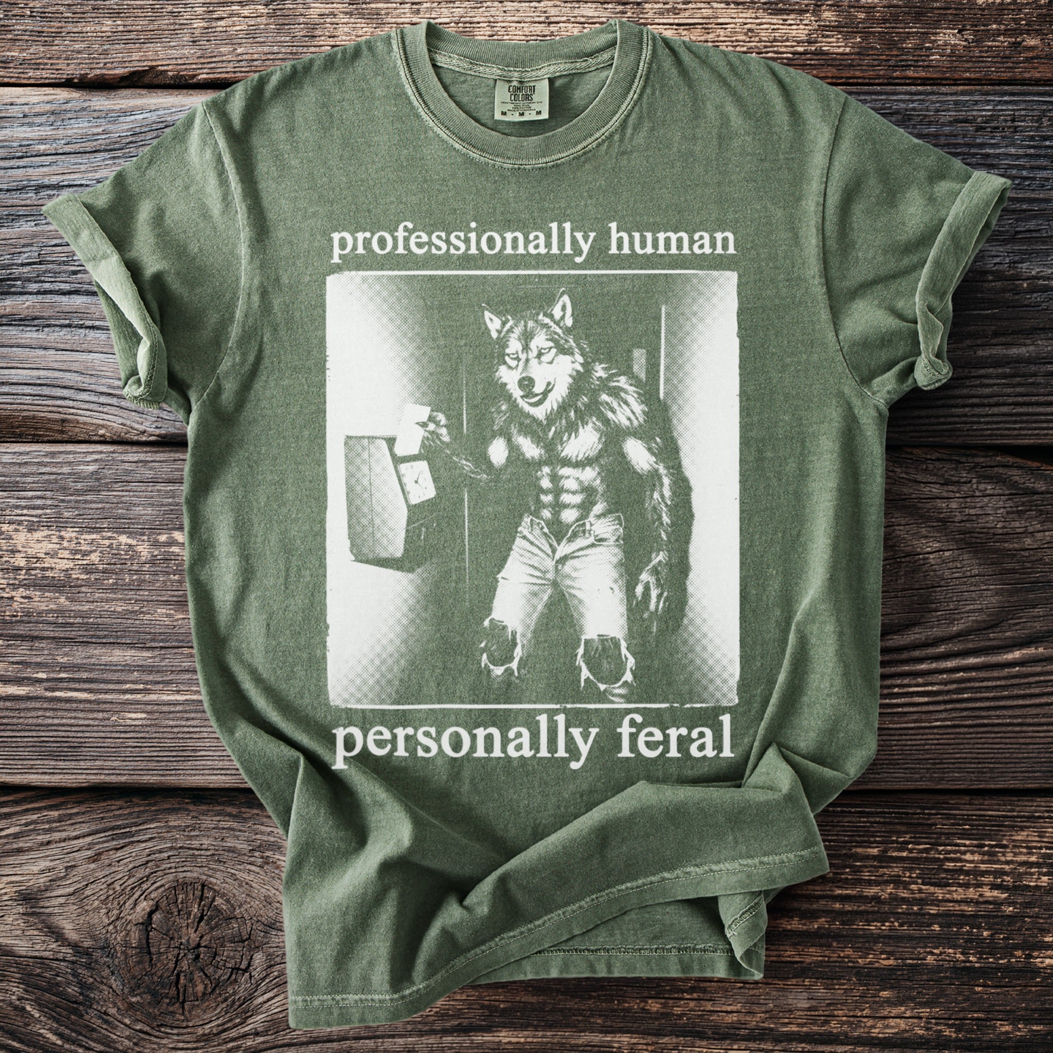 Olive green t-shirt with wolf graphic and text "professionally human personally feral".