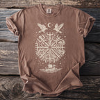 Brown t-shirt with a cream-colored circular design featuring ravens, a moon, a Viking ship, and rune-like symbols.