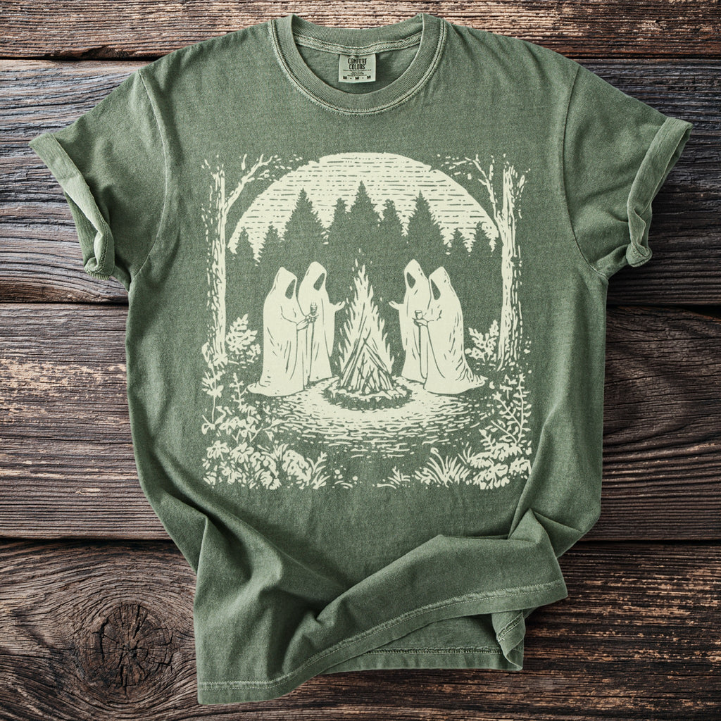 Green t-shirt with a cream graphic of cloaked figures around a campfire in a forest.