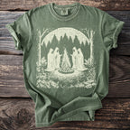 Green t-shirt with a cream graphic of cloaked figures around a campfire in a forest.
