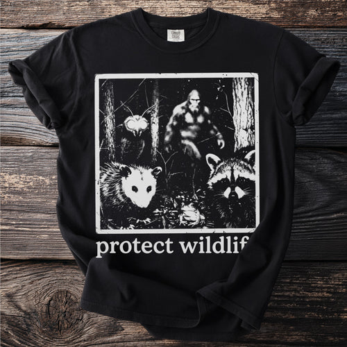 Black t-shirt with a graphic of Bigfoot, opossum, raccoon, moth, and frog. Text says "protect wildlif".