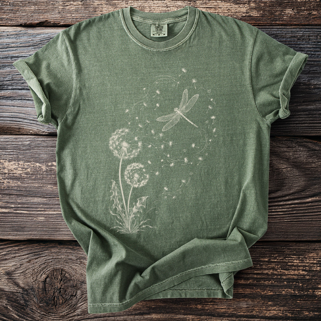 Green t-shirt with white dandelion and dragonfly graphic on a wooden background.