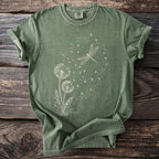 Green t-shirt with white dandelion and dragonfly graphic on a wooden background.