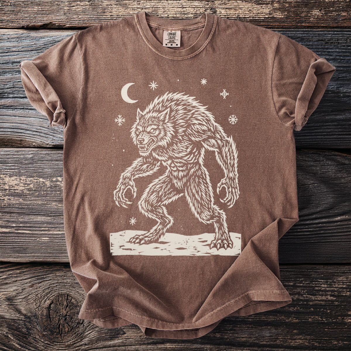 Espresso brown t-shirt with a cream folk-cut print: a hunched werewolf, teeth bared and claws out, stands in the snow under a crescent moon.