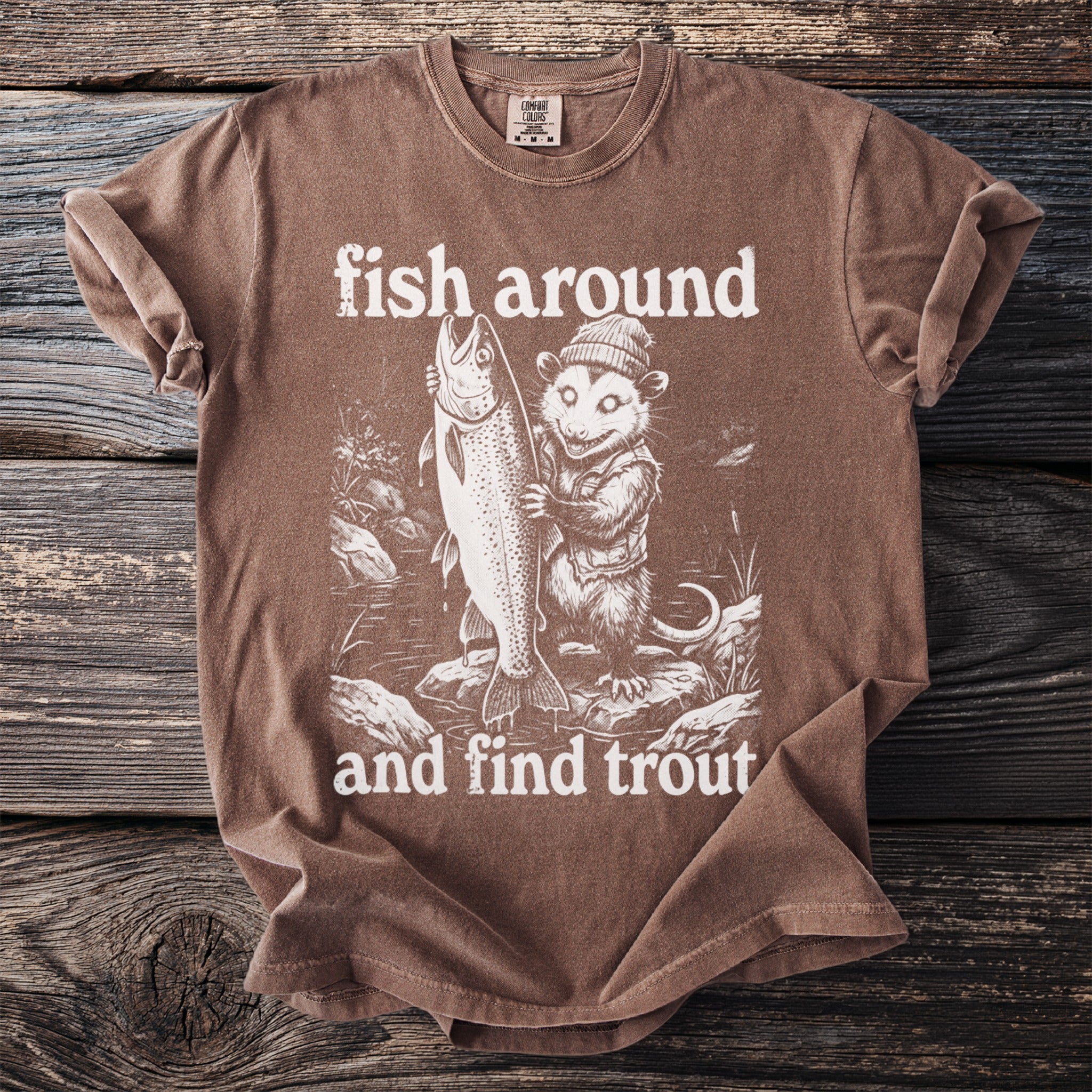Brown t-shirt with graphic of a possum holding a large trout, text "fish around and find trout".