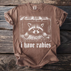 Brown t-shirt with a graphic of a raccoon and the words "i have rabies".