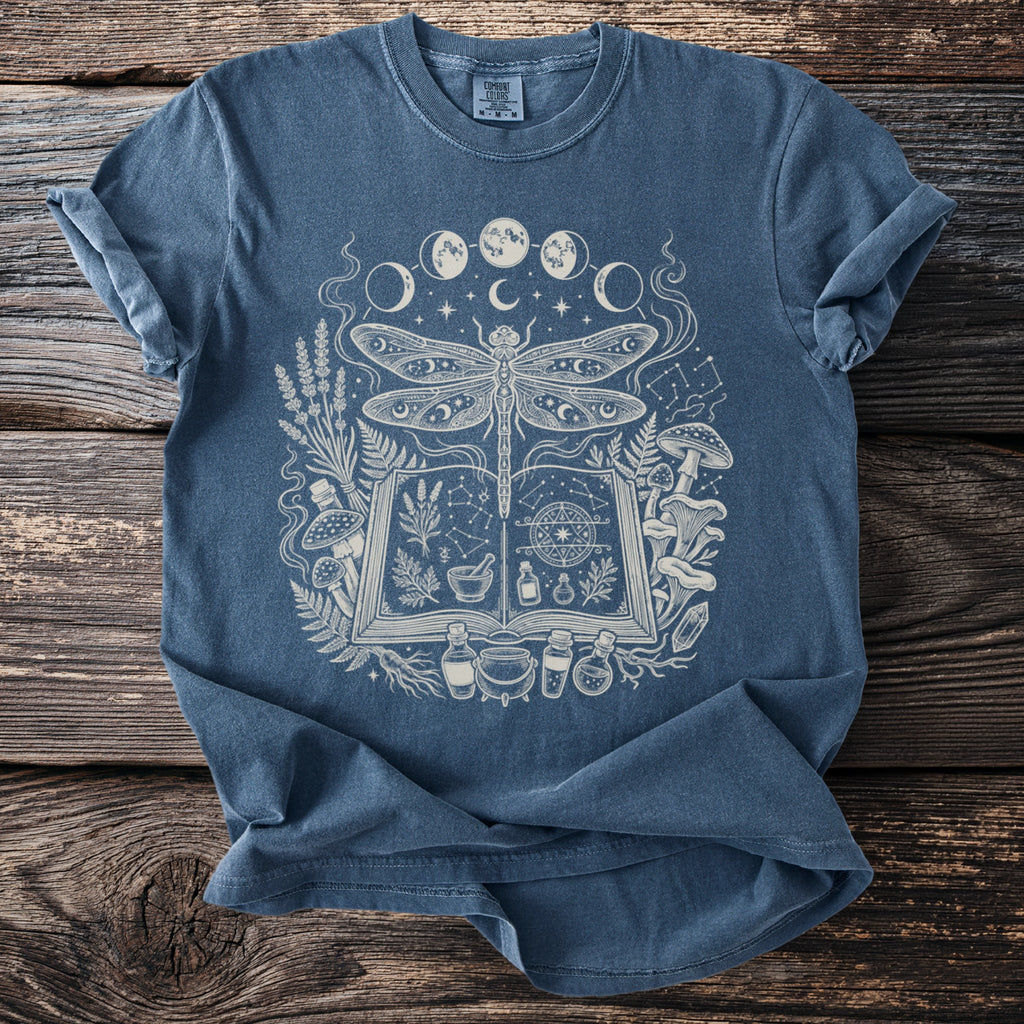 Blue t-shirt with a white graphic of a dragonfly over an open book and mystical elements.