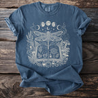 Blue t-shirt with a white graphic of a dragonfly over an open book and mystical elements.