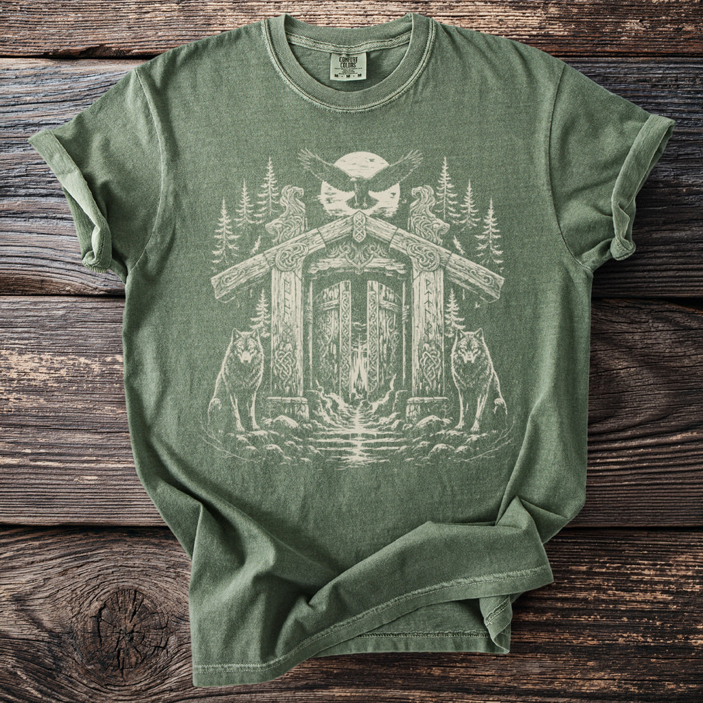Green t-shirt with a light beige graphic of wolves, an eagle, and a wooden gate.
