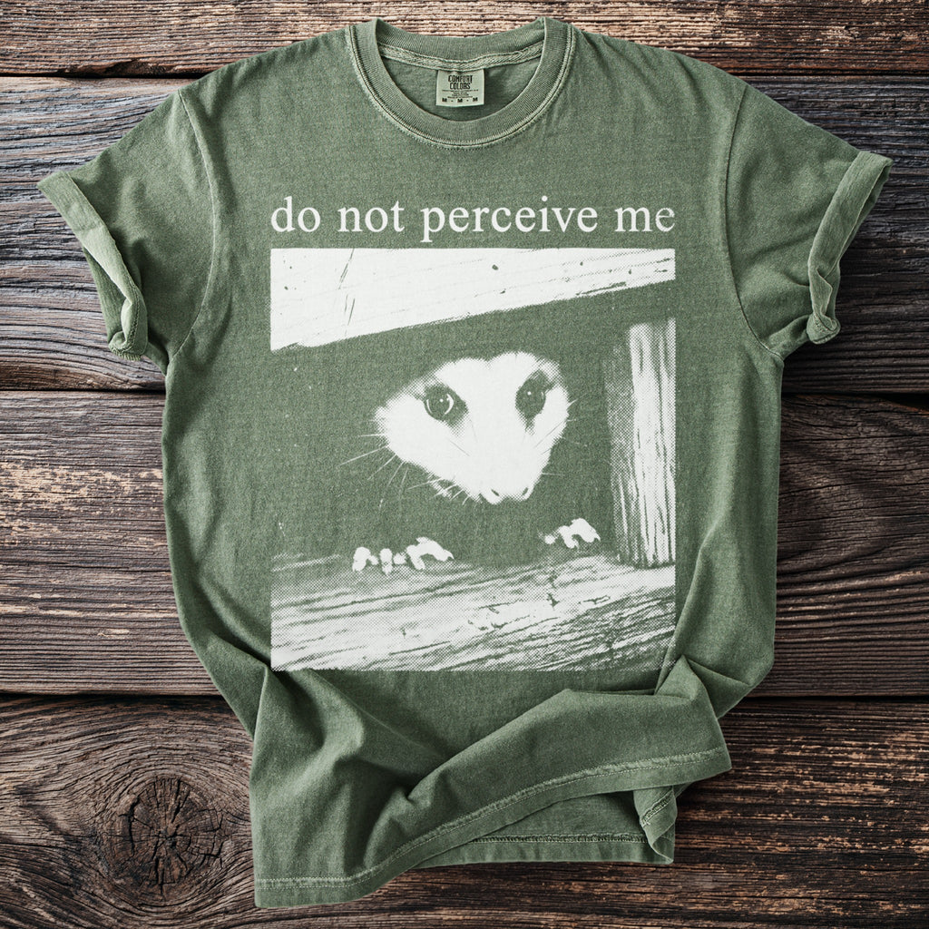 Green t-shirt with an opossum peeking out and text "do not perceive me".