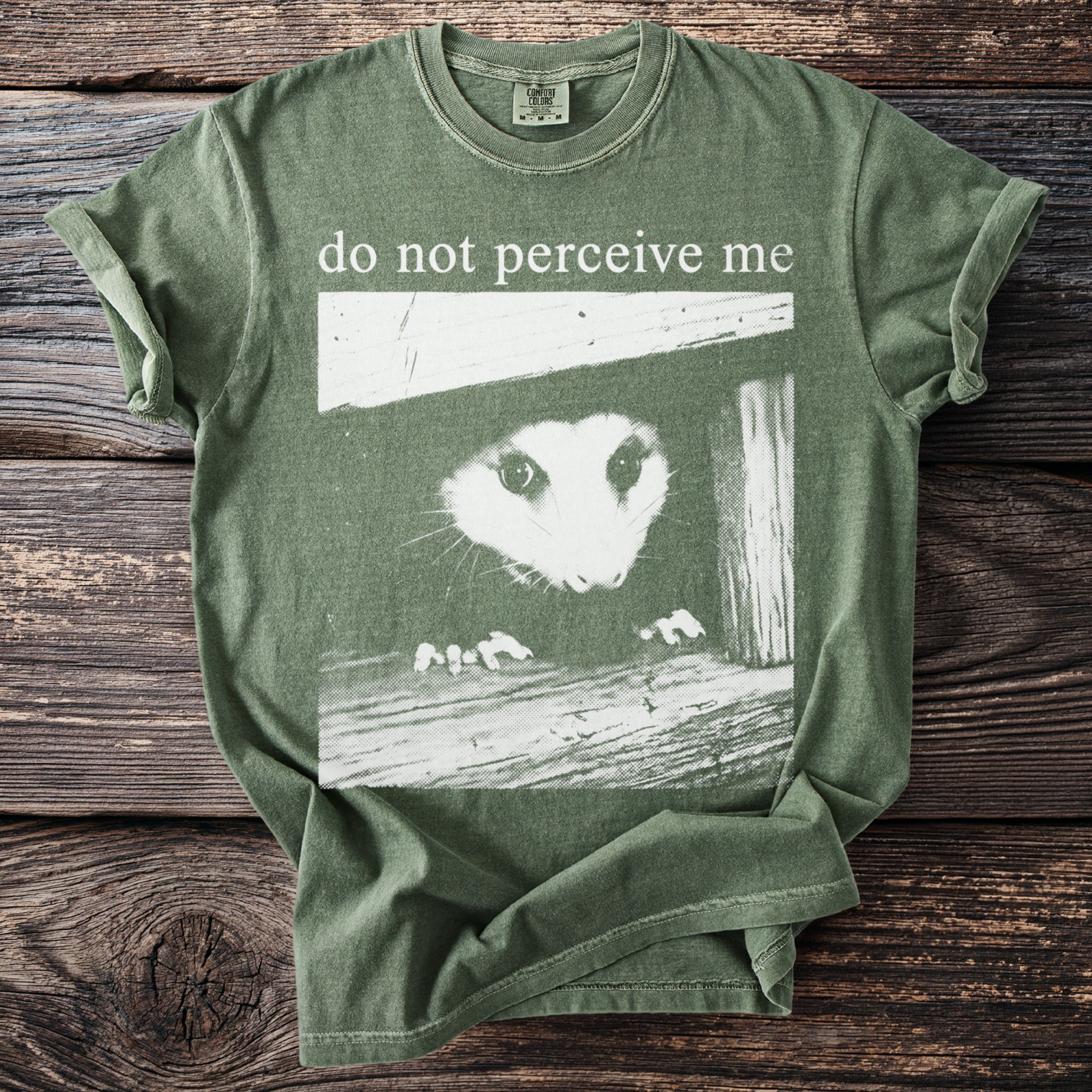 Green t-shirt with an opossum peeking out and text "do not perceive me".