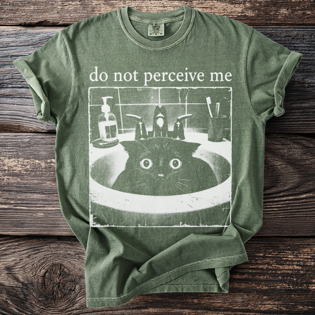 Green t-shirt with "do not perceive me" and a startled cat in a sink graphic.