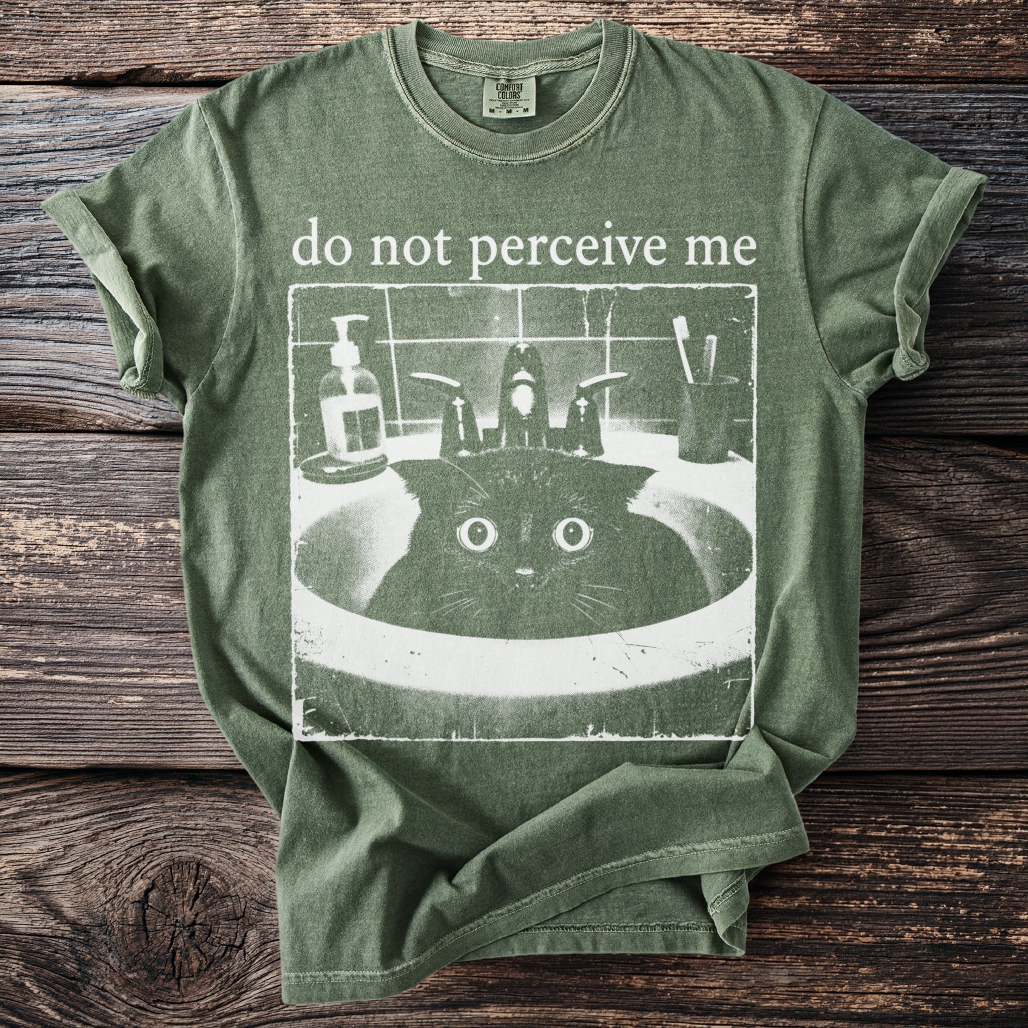 Green t-shirt with "do not perceive me" and a startled cat in a sink graphic.