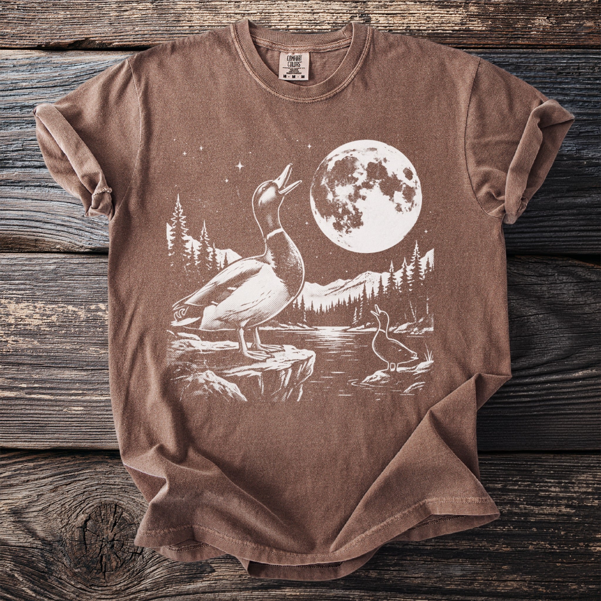 Brown comfort colors t-shirt with white graphic of two ducks, moon, and mountains.