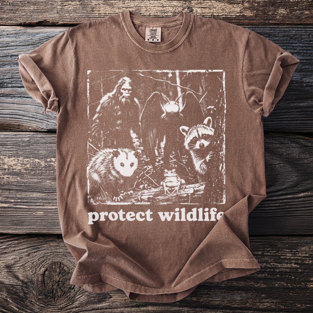 Brown t-shirt with graphic of Bigfoot, owl, raccoon, opossum, and frog with "protect wildlife" text.