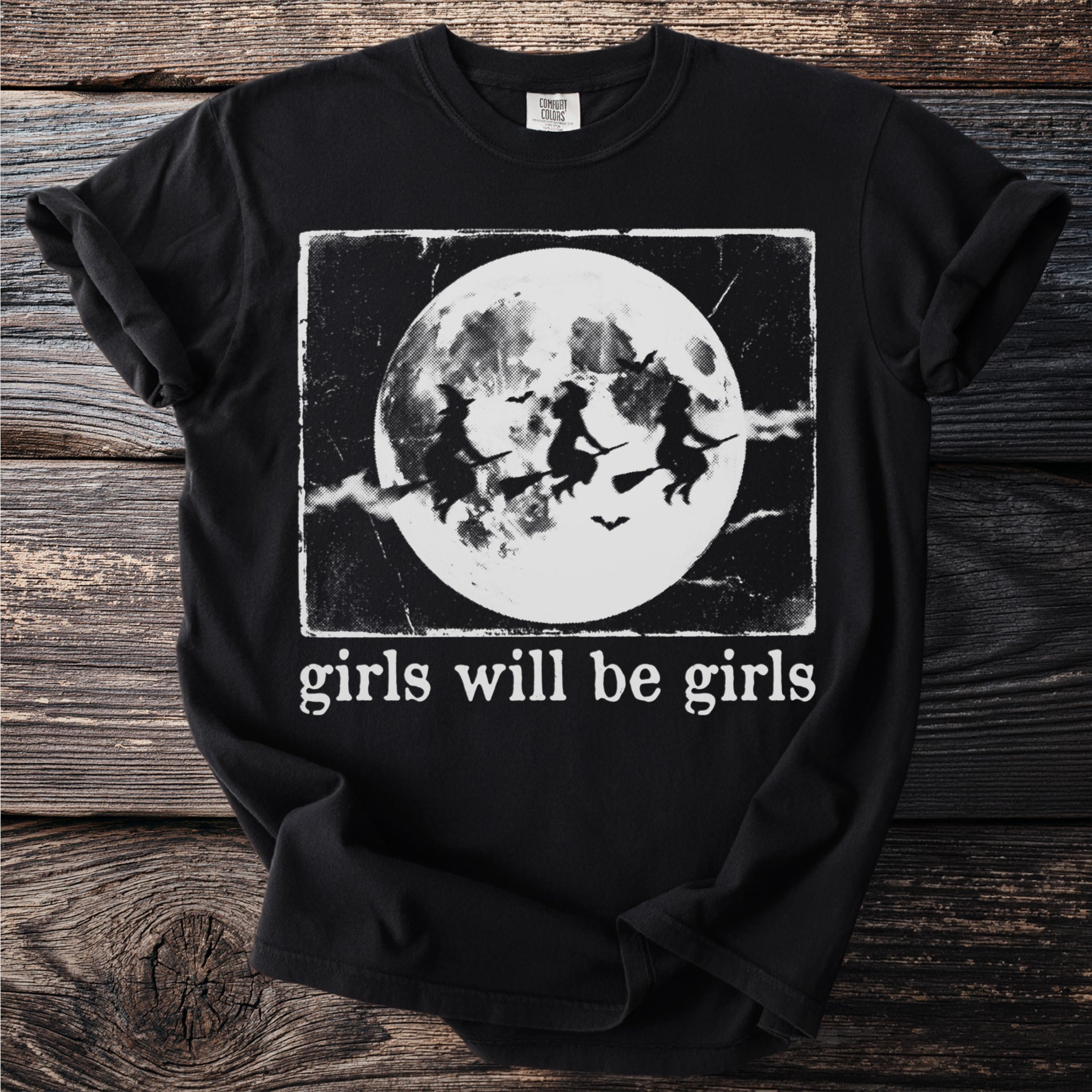Black t-shirt with flying witches and "girls will be girls" text.