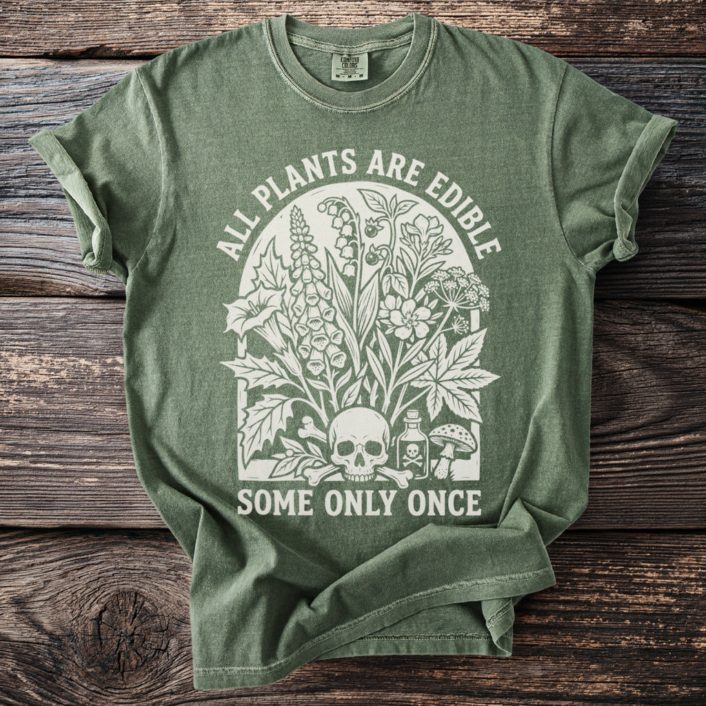Green t-shirt with white graphic of plants, skull, bones, and text: "ALL PLANTS ARE EDIBLE SOME ONLY ONCE".