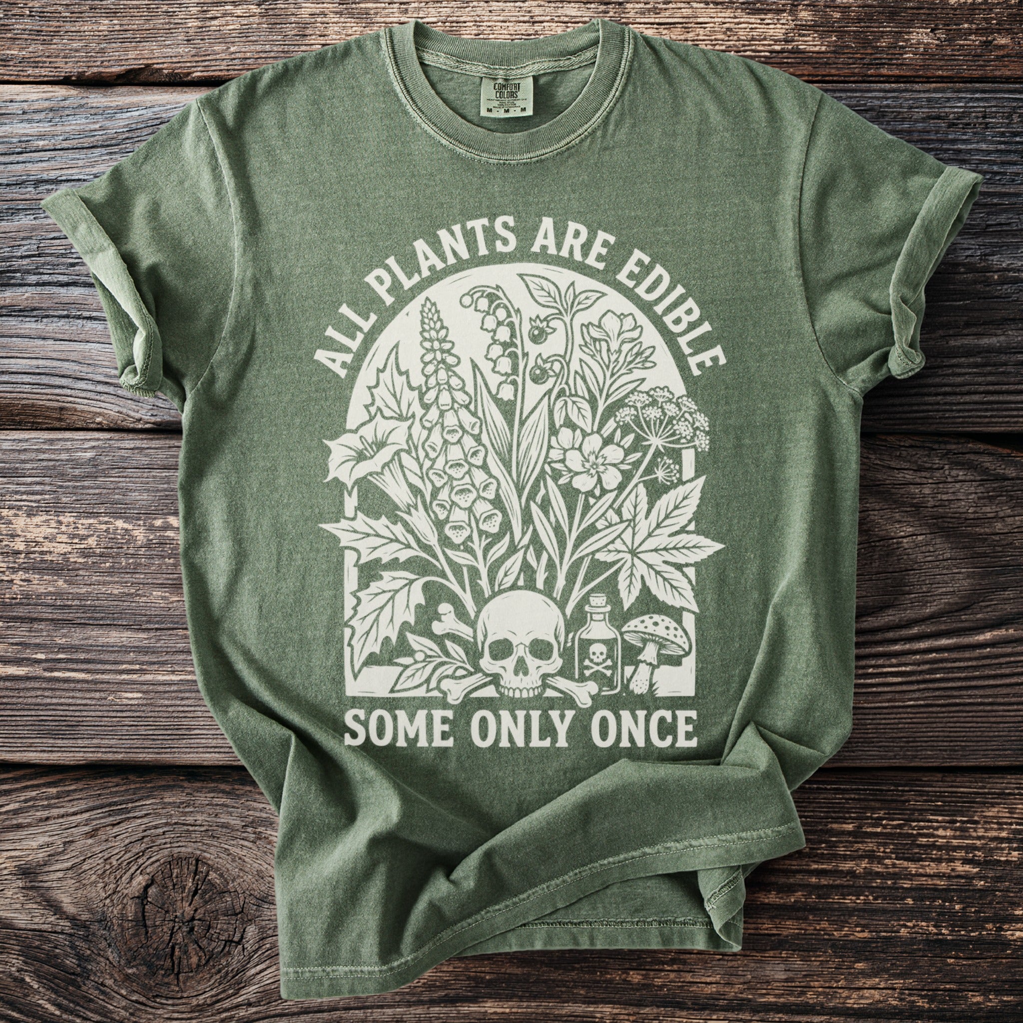 Green t-shirt with white graphic of plants, skull, bones, and text: "ALL PLANTS ARE EDIBLE SOME ONLY ONCE".
