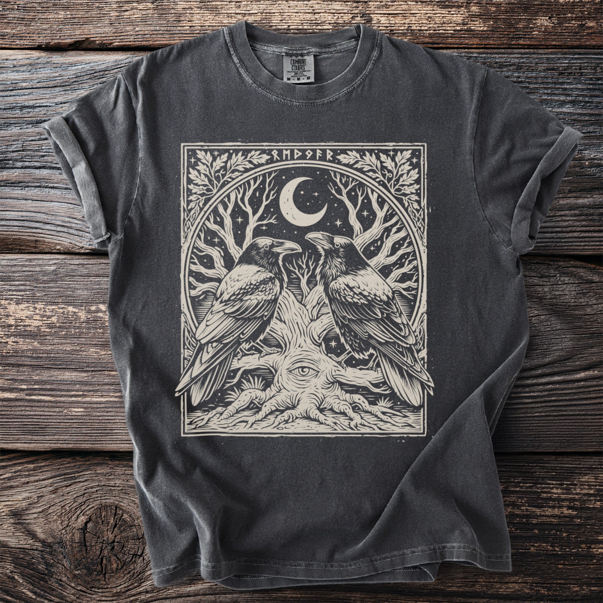 Dark grey t-shirt with a circular graphic of two ravens, a crescent moon, star, and an eye within a tree.