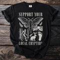Black t-shirt with "Support Your Local Cryptids" text and illustrations of Bigfoot, Mothman, and a jackalope.