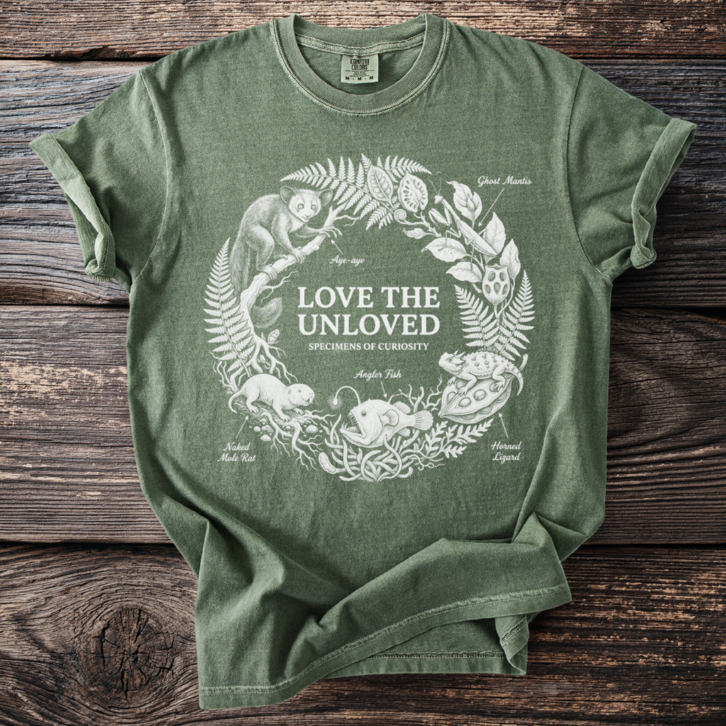 Green t-shirt with "Love the Unloved Specimens of Curiosity" text and illustrations of unusual creatures.