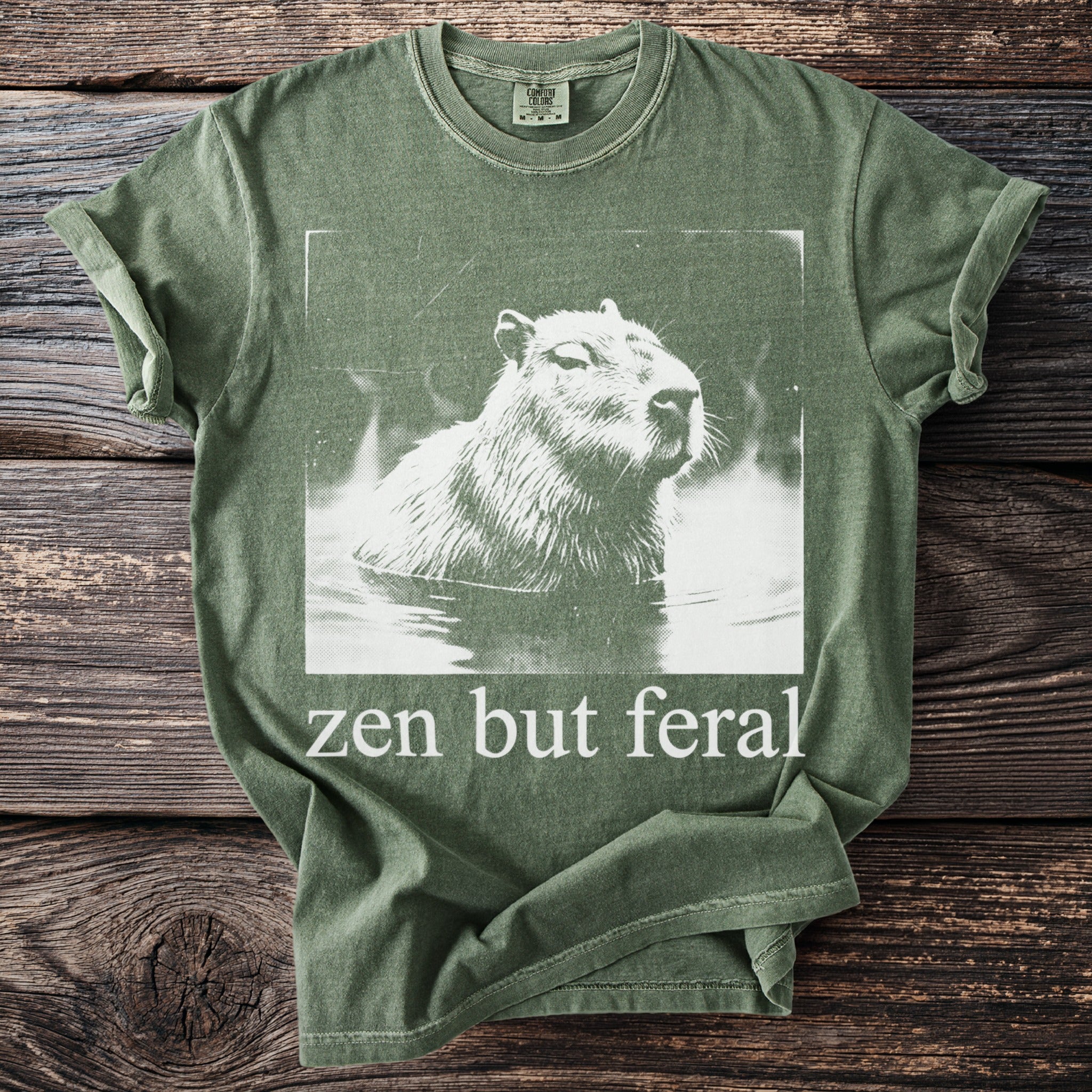 Green t-shirt with white capybara graphic and text "zen but feral".