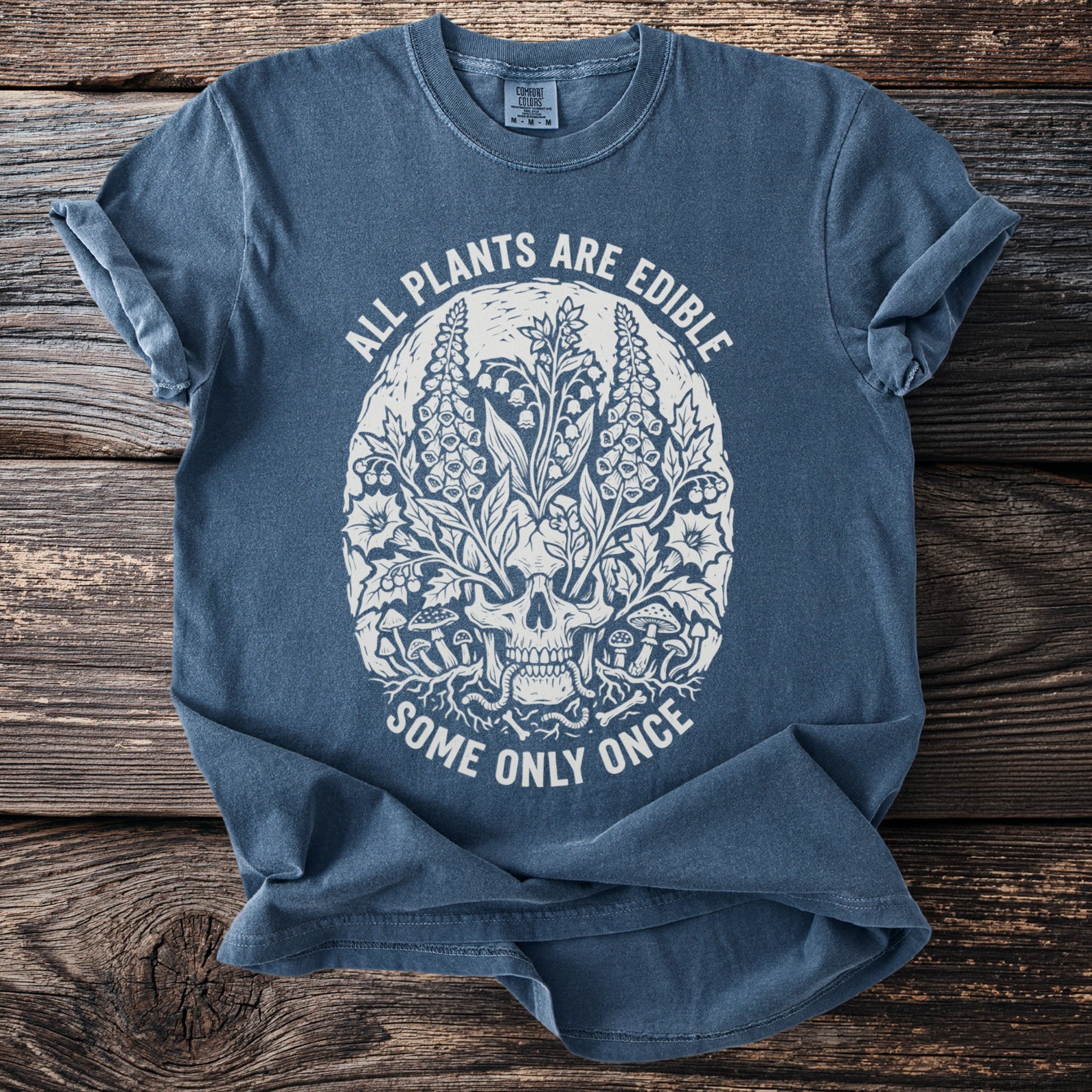 Blue t-shirt with skull and plant graphic: "ALL PLANTS ARE EDIBLE SOME ONLY ONCE"