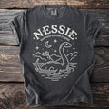Dark gray t-shirt with white graphic of Nessie, Loch Ness, castle on wooden background.