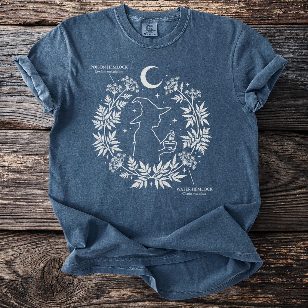 Blue t-shirt with white graphics of a witch silhouette and botanical designs, featuring text for poison and water hemlock.
