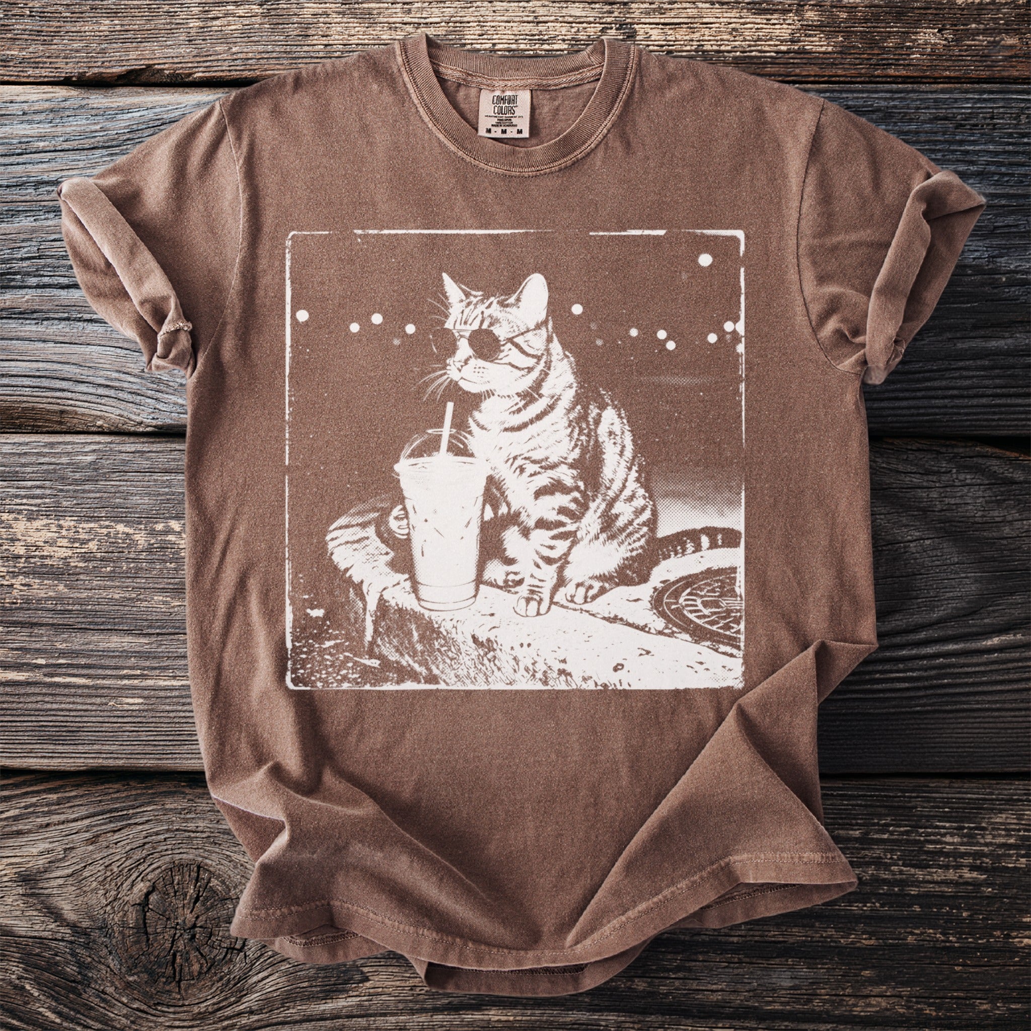 Brown t-shirt with white graphic of a cat drinking an iced beverage, wearing sunglasses.