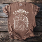Brown t-shirt with white graphic of three-headed Cerberus and text "CERBERUS greek mythology underworld hound".
