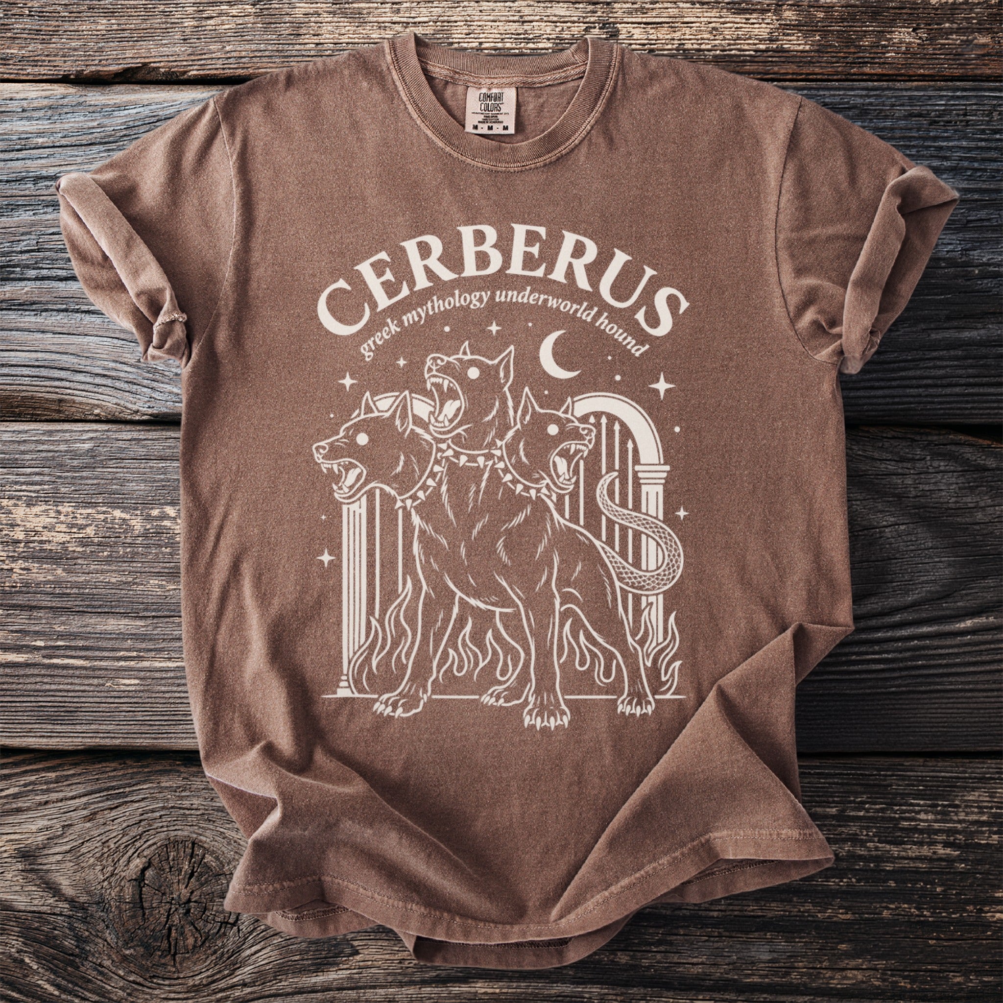 Brown t-shirt with white graphic of three-headed Cerberus and text "CERBERUS greek mythology underworld hound".