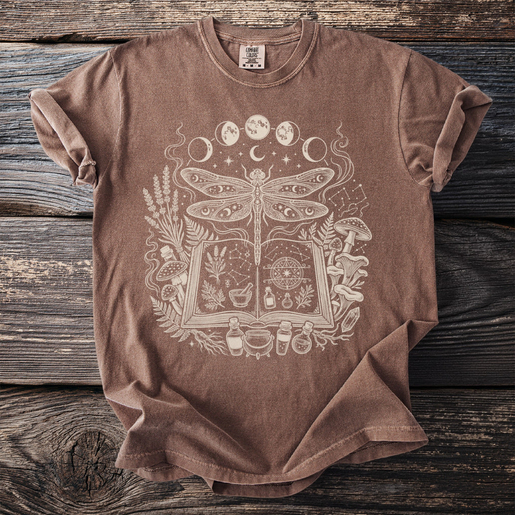 Brown t-shirt with white mystical dragonfly, moon phases, and potion ingredients graphic.