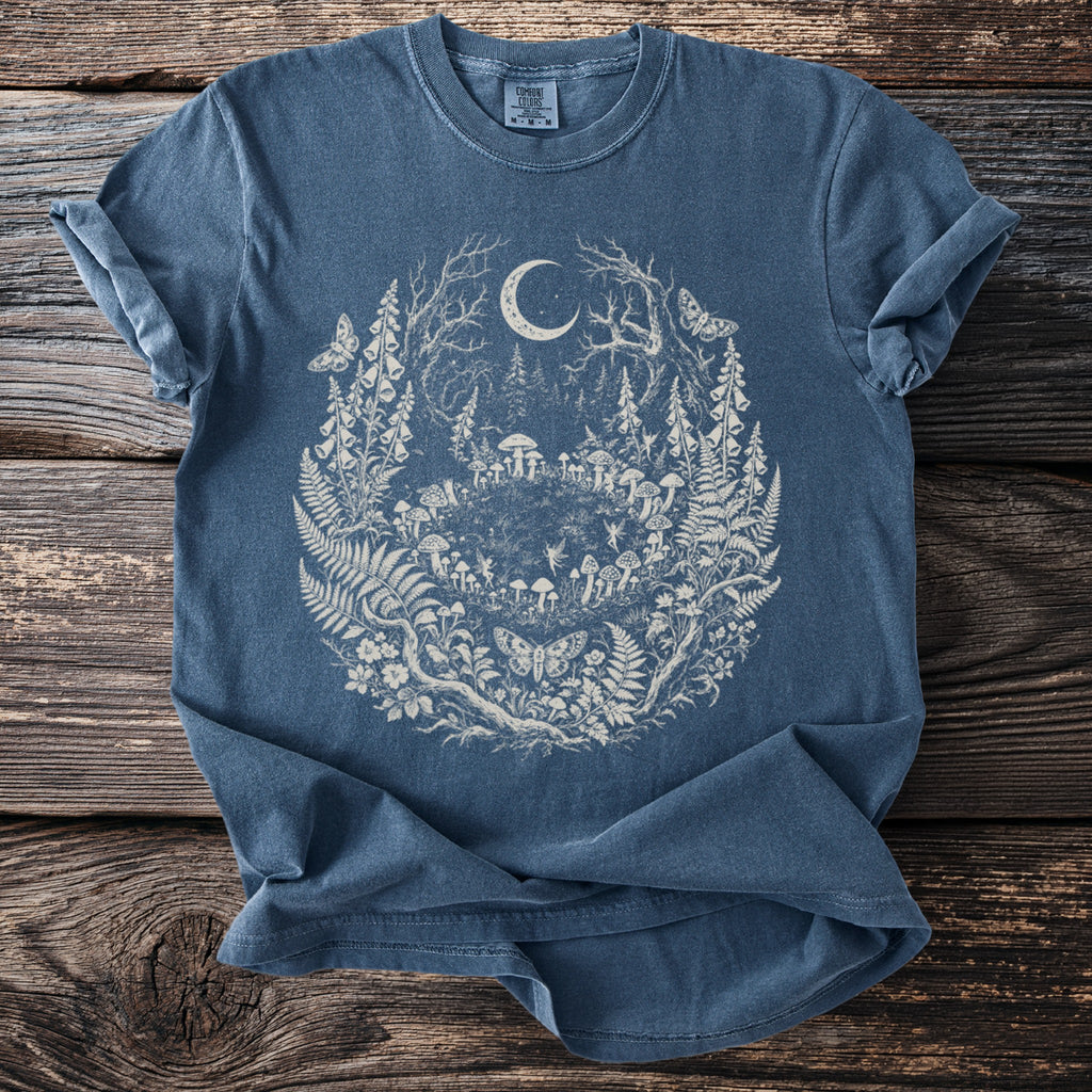 Blue t-shirt with a circular forest design featuring a crescent moon, mushrooms, fairies, and butterflies.
