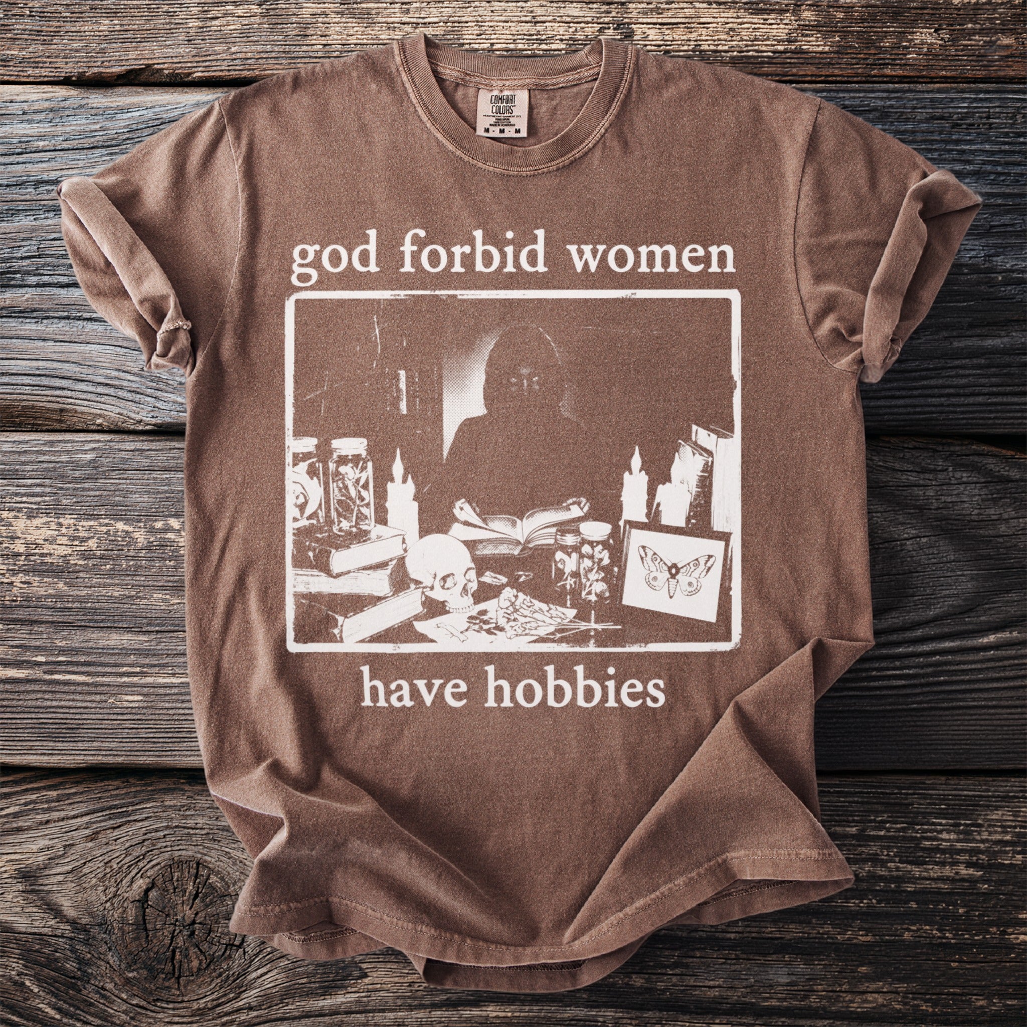 Brown t-shirt with "god forbid women have hobbies" text and graphic.