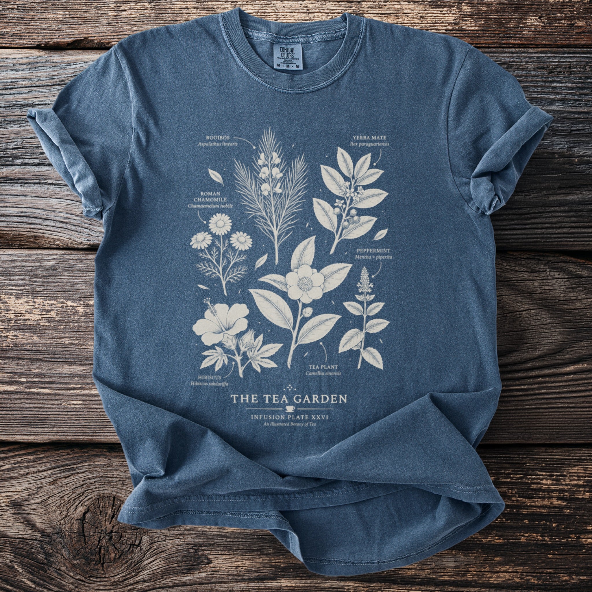 Blue t-shirt with botanical illustrations of tea ingredients and the text "The Tea Garden".