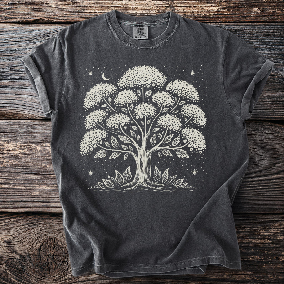Dark gray t-shirt with a cream linocut print of a stylized tree under a crescent moon.