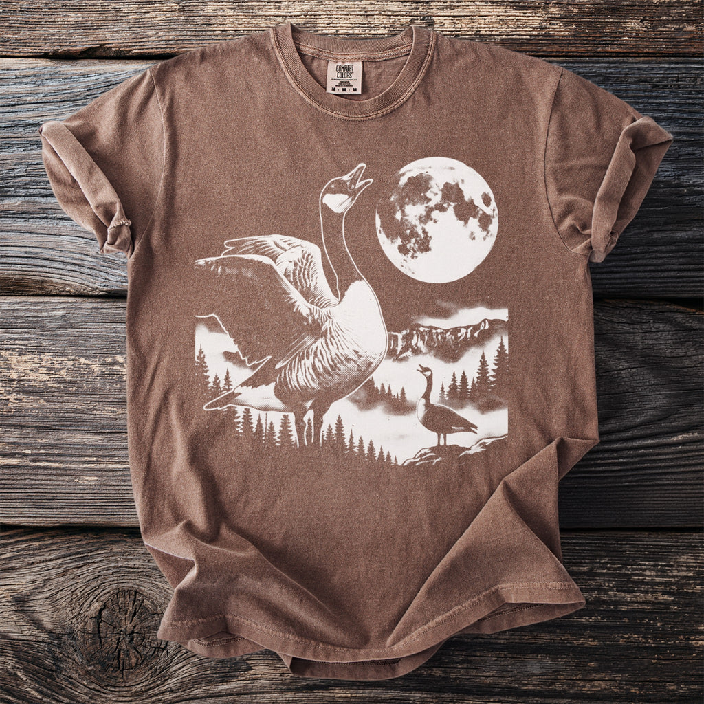 Brown t-shirt with a graphic of geese, mountains, trees, and a full moon.