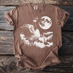 Brown t-shirt with a graphic of geese, mountains, trees, and a full moon.